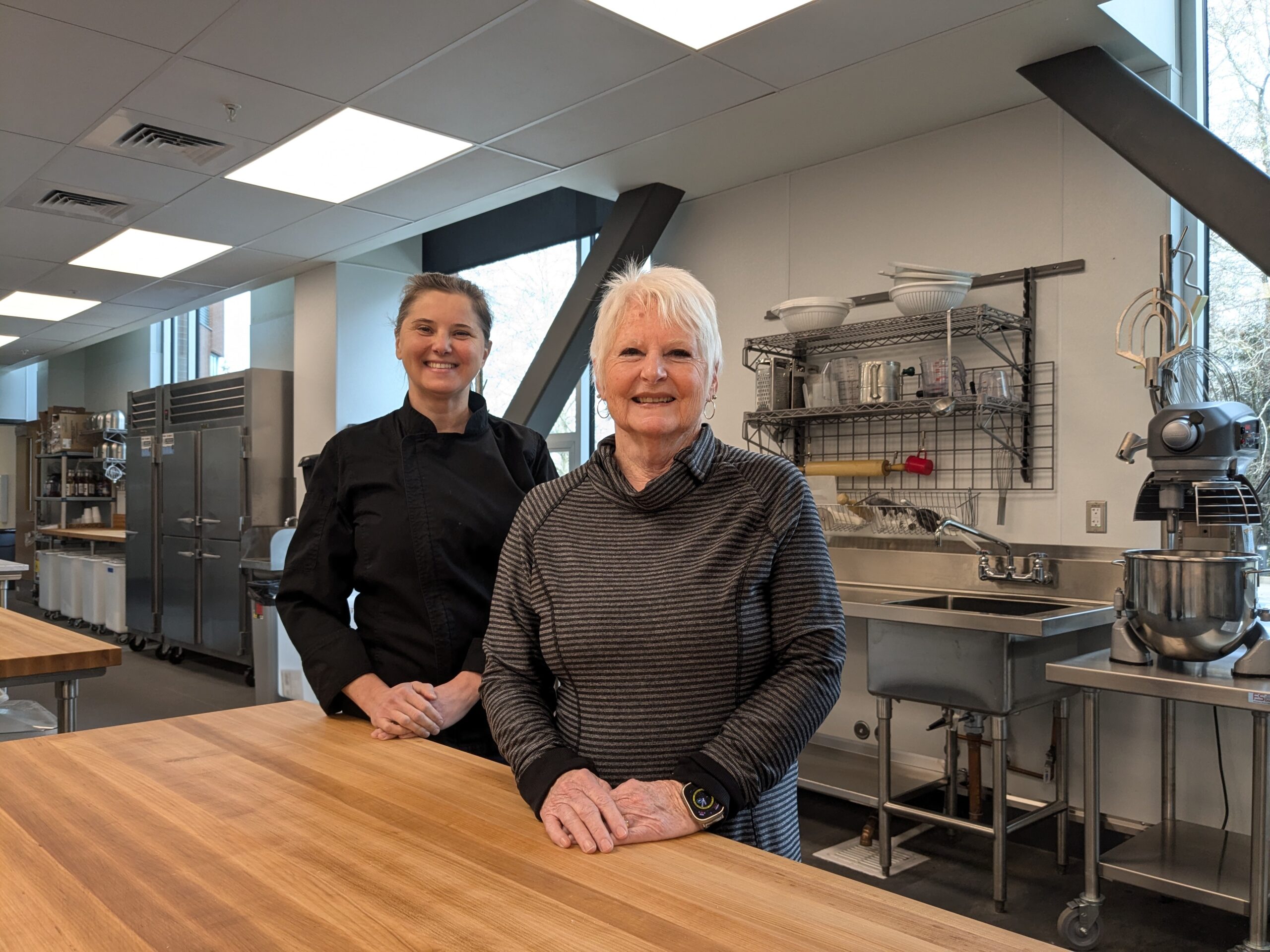 Chef Nina Urioste (left) and Candi Bachtell (right) stand in Grays Harbor College's new culinary kitchen, surrounded by stainless steel appliances and professional cooking stations.