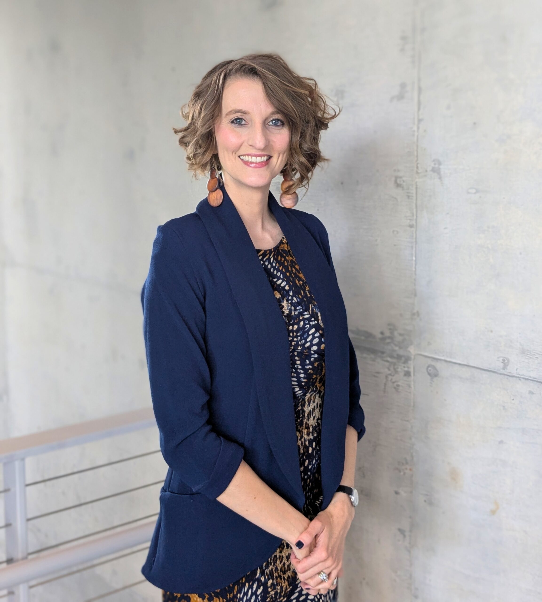 Executive Director Lisa J. Smith standing against a gray wall, wearing a blue outfit, smiling warmly.
