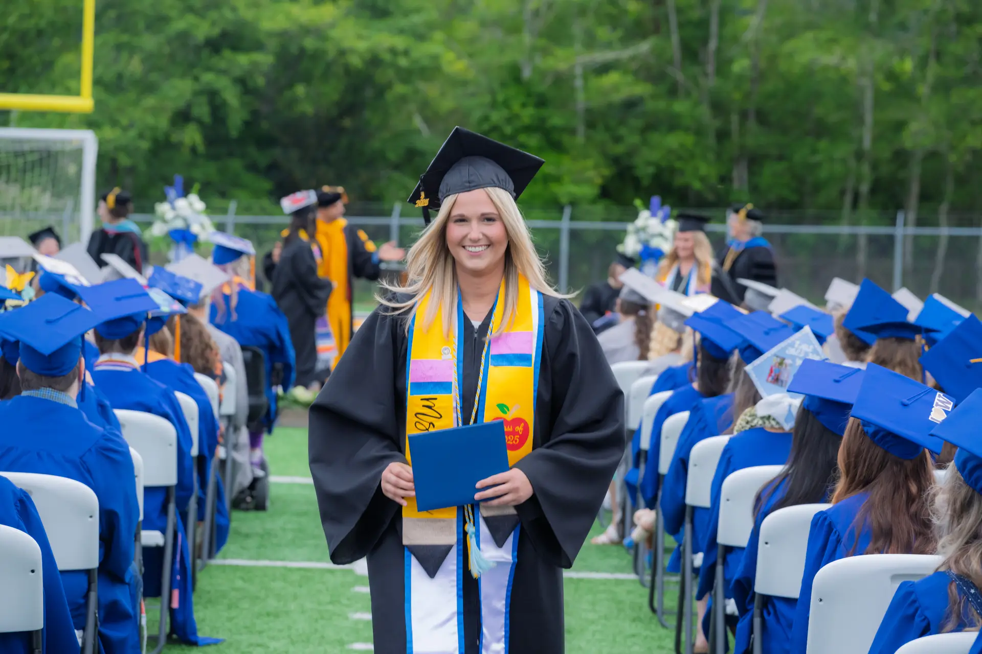 Graduate walking down an aisle at an outdoor commencement ceremony.
